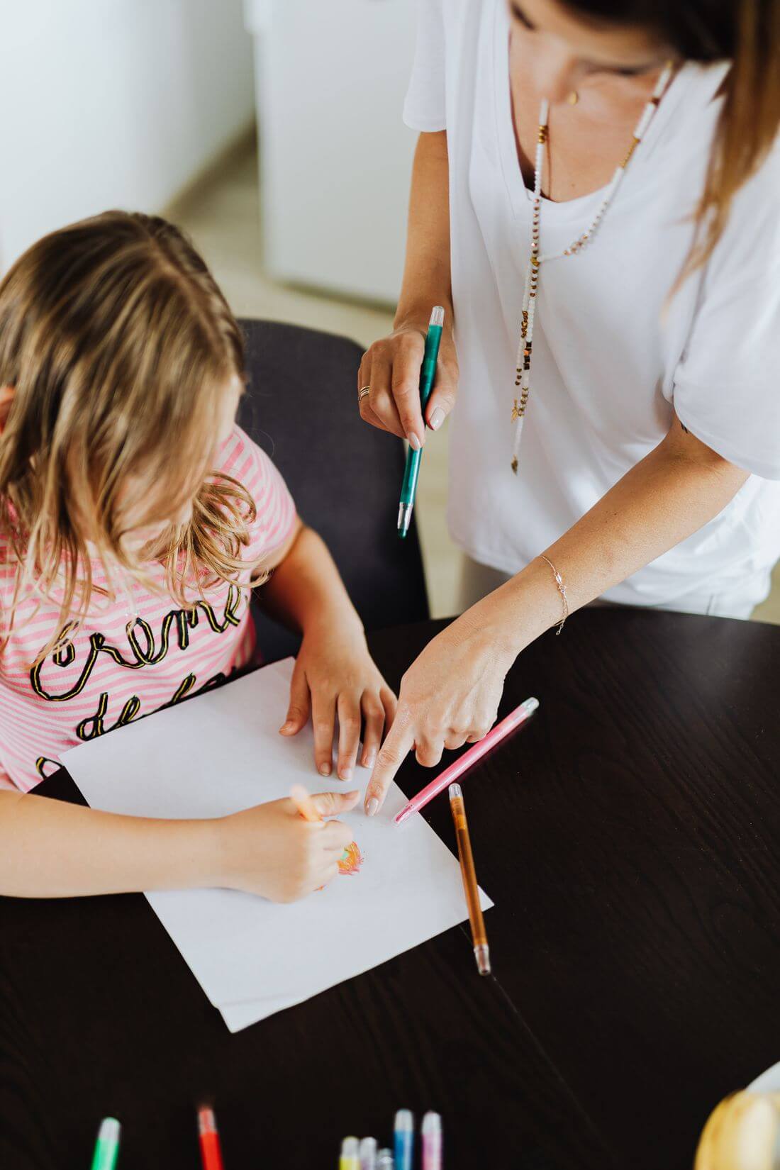 Una babysitter aiuta una bambina a disegnare con i pennarelli al tavolo