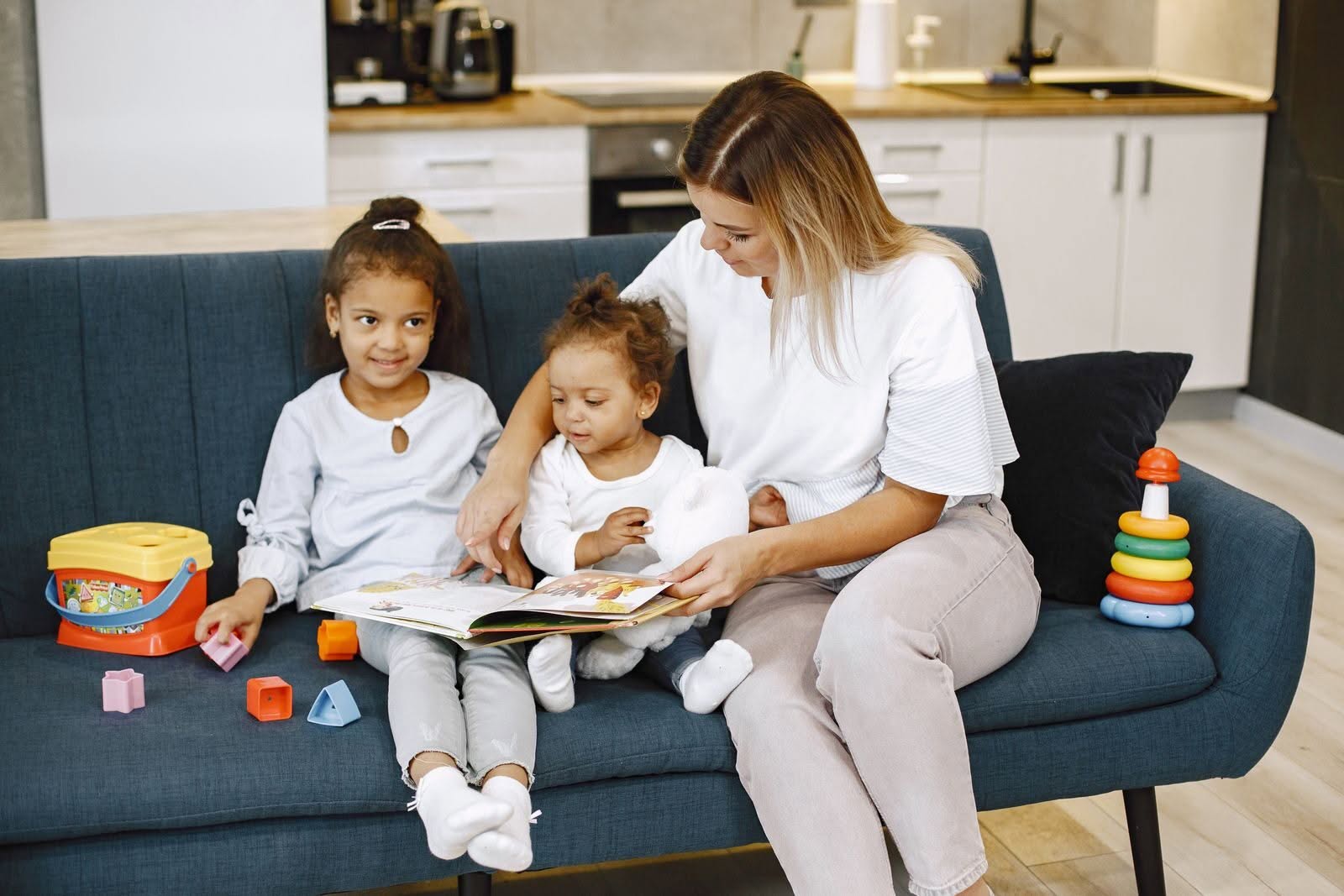 Una babysitter legge un libro a due bambini seduti sul divano di casa